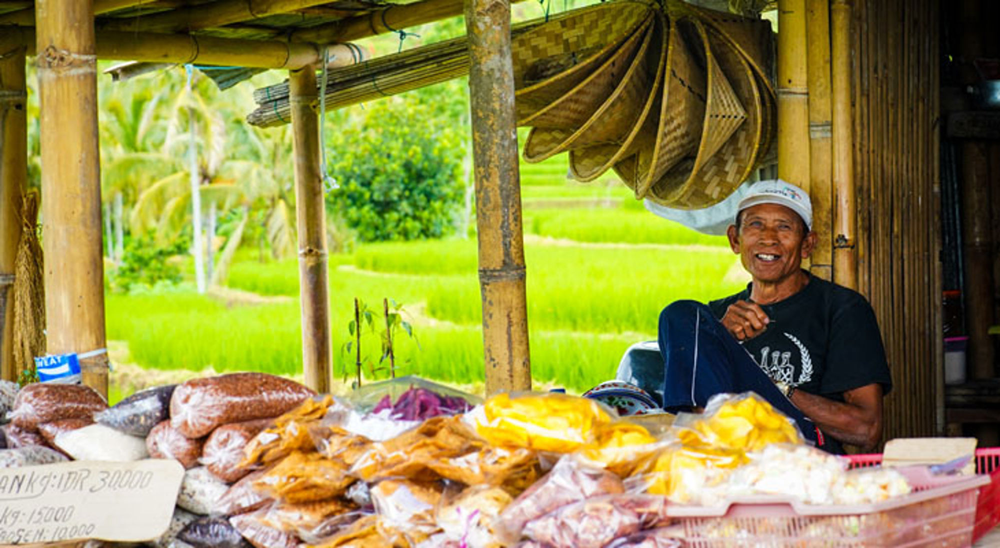 Village Jatiluwih Indonesië Indonesische marktverkoper in bamboekraam met snacks, met groene rijstvelden op de achtergrond.