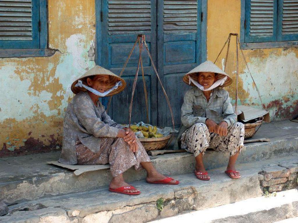 Twee reizigers met hoeden kijken uit over een rivierlandschap tijdens een groepsrondreis Vietnam kort.