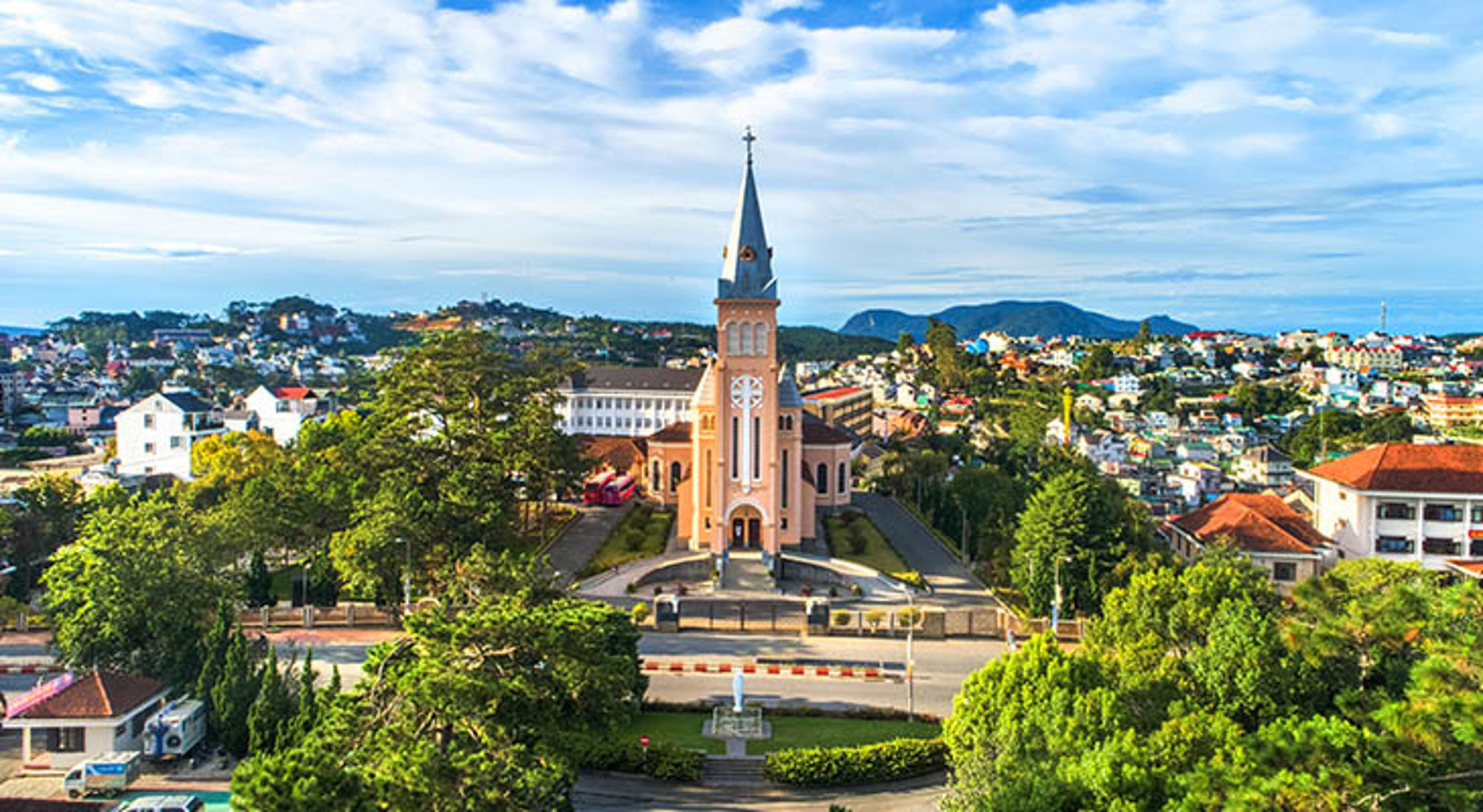 Roze kathedraal met hoge torenspits in Da Lat, Vietnam, omringd door groen en stadshuisjes.