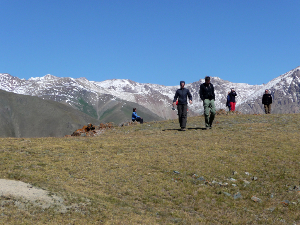 Wandelaars tijdens groepsrondreis Kirgistan op een bergplateau met besneeuwde toppen op de achtergrond.