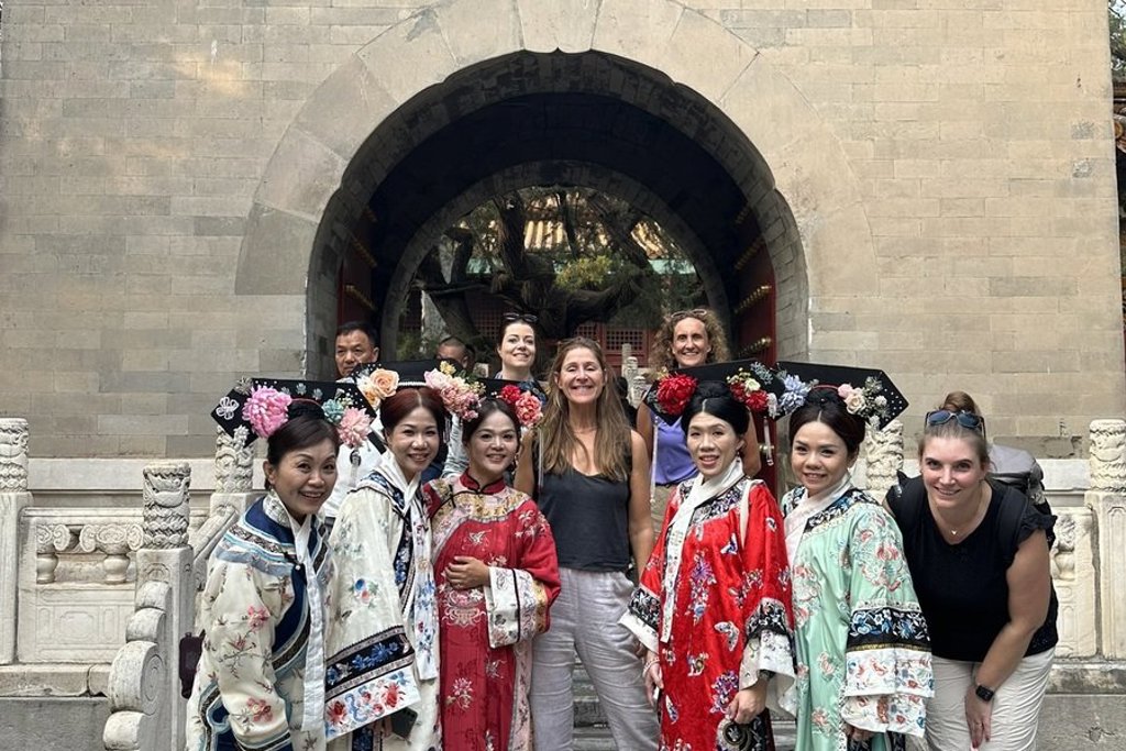 Groepsrondreis China: reizigers poseren met vrouwen in traditionele klederdracht bij een historische poort.