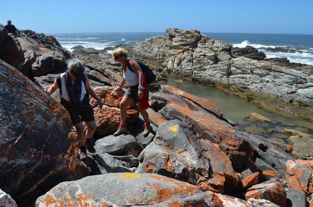 Wandelaars op rotsachtige kustlijn langs de Tuinroute in Zuid-Afrika, met uitzicht op de oceaan.