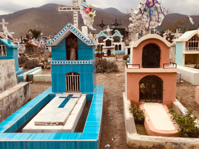 Kleurrijke graven op een begraafplaats in Peru, met bergen op de achtergrond.