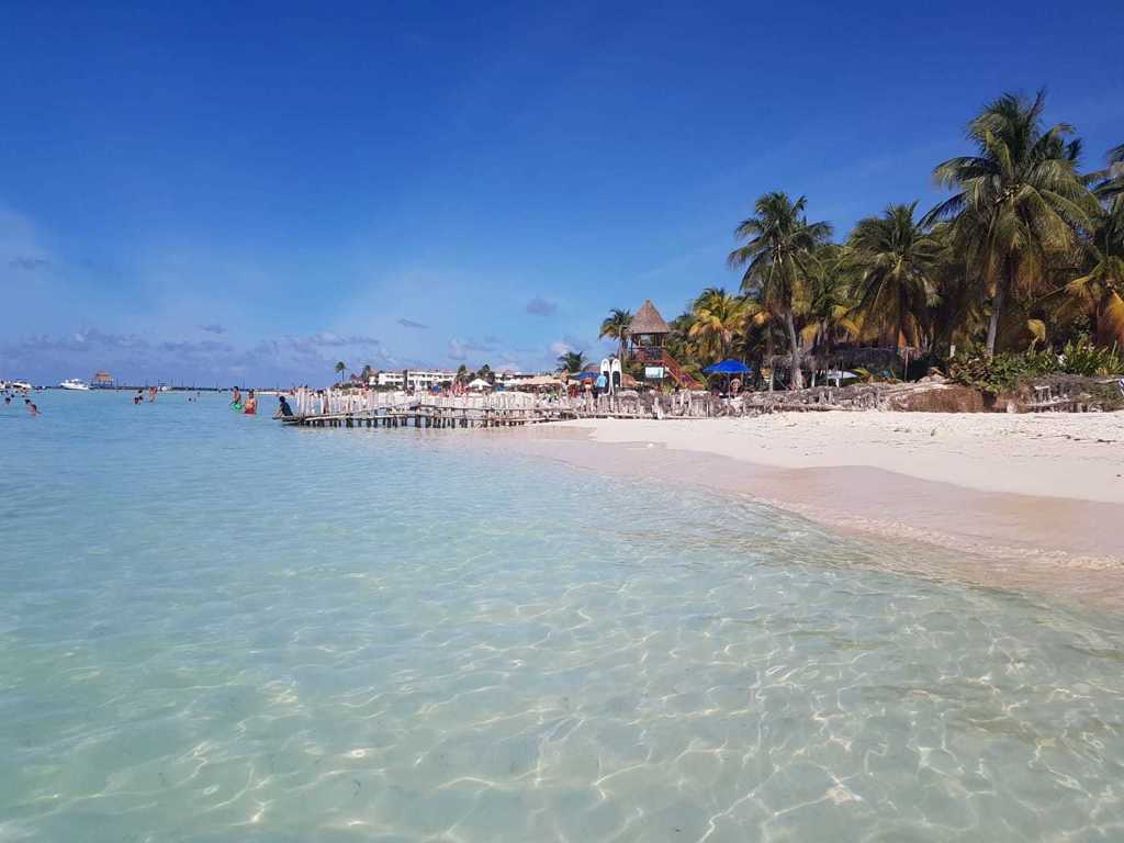 Wit zandstrand met palmbomen en helderblauw water aan de Caribische kust van Mexico tijdens een groepsrondreis.