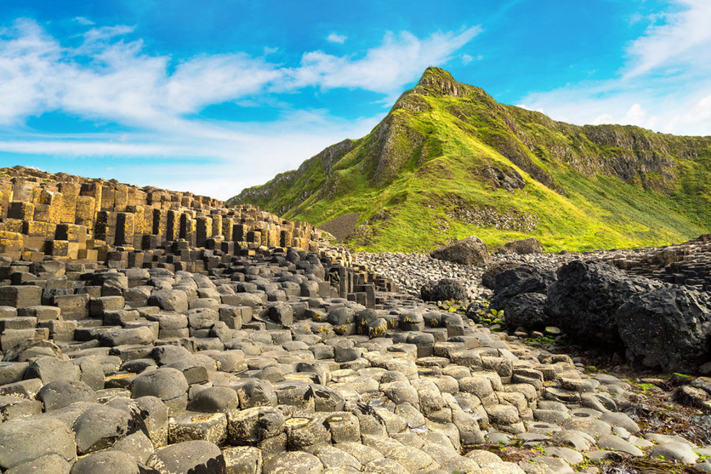 Giant’s Causeway met basaltzuilen aan de kust van Noord-Ierland, met groene heuvels op de achtergrond.