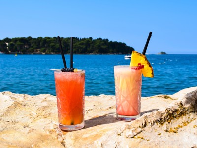 Twee zomerse cocktails op rotsen aan zee met eiland op de achtergrond, route Balkan.