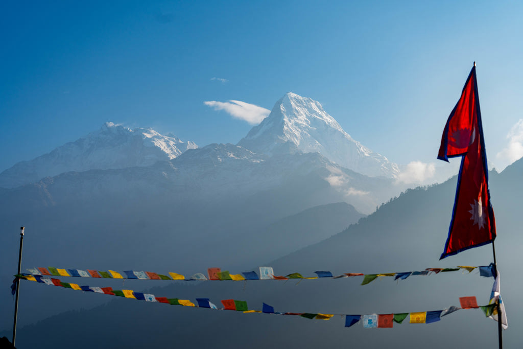 Nepalese vlag en gebedsvlaggetjes met besneeuwde Himalaya-berg op de achtergrond tijdens 22-35ers reis Nepal.