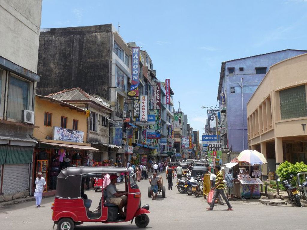 Drukke straat in Colombo, Sri Lanka, met tuk-tuk, winkels en kleurrijke reclameborden.
