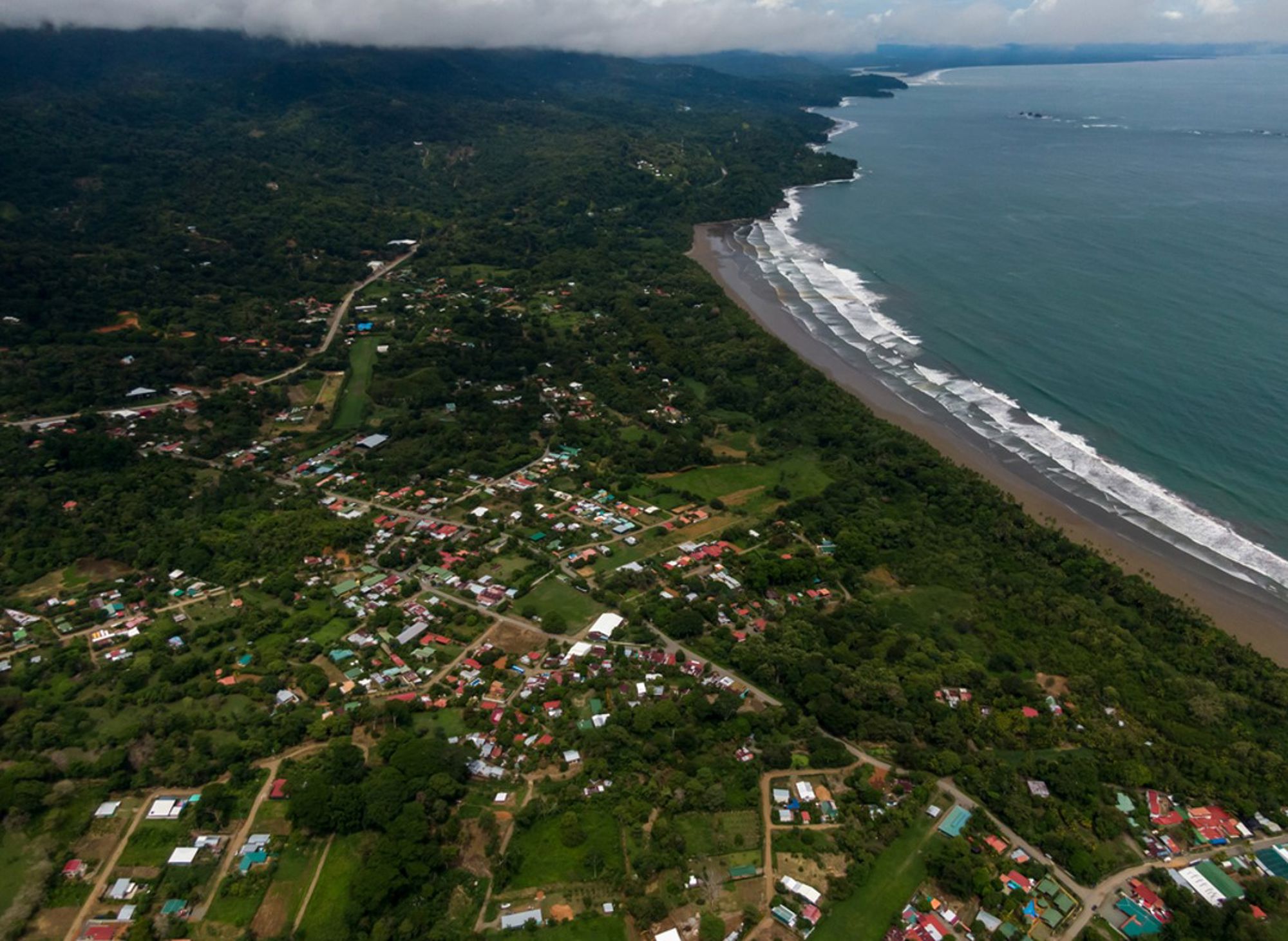 de Pacifische kustlijn in Costa Rica met een dorp in het groen en een lang zandstrand.
