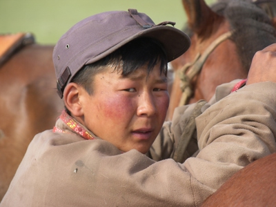 Jonge ruiter met pet bij een paard tijdens de Mongolië Naadam festivalreis.