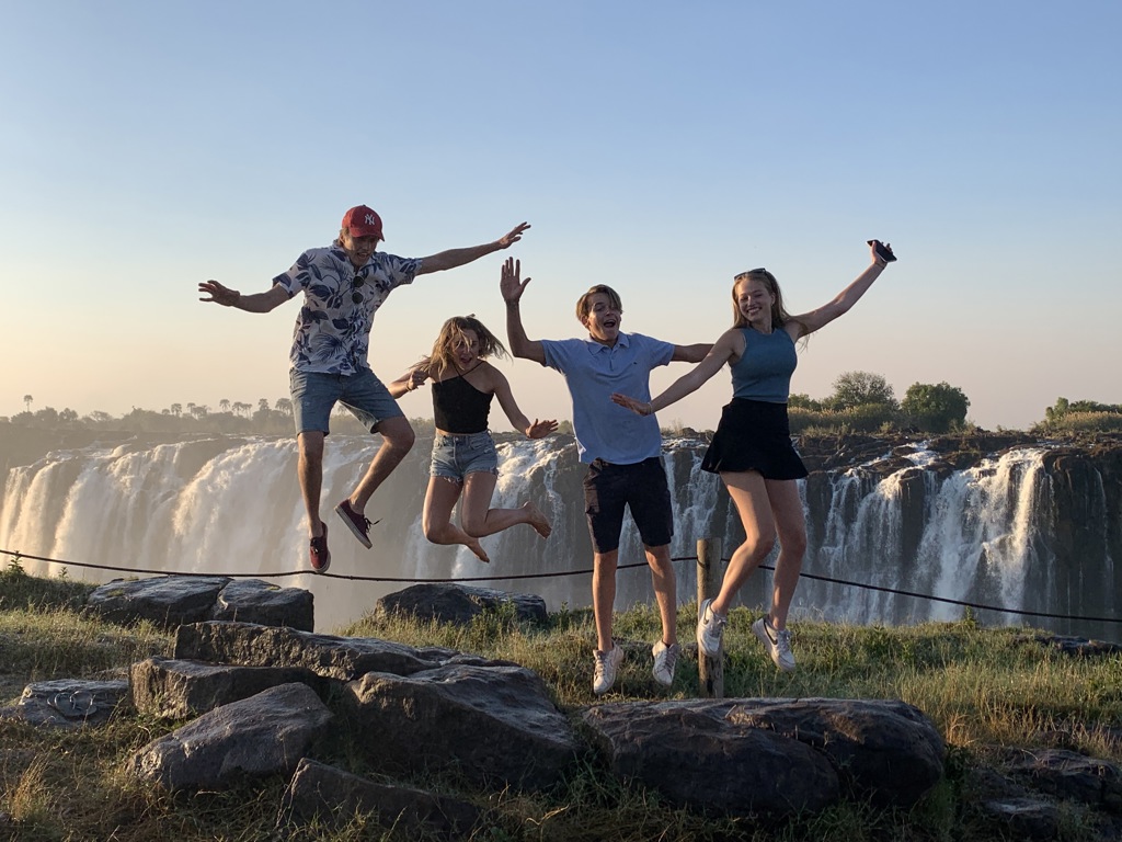 Gezin springt van blijdschap bij de Victoriawatervallen tijdens een familiereis Namibië, Botswana en Zimbabwe.