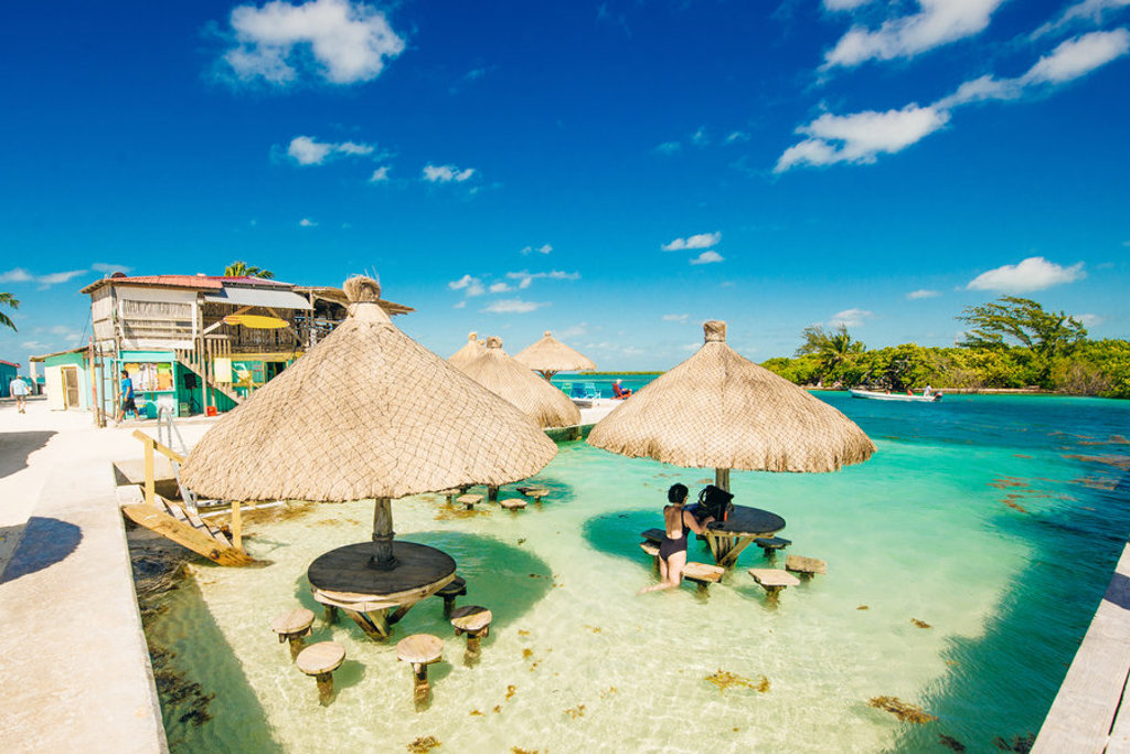 Strandbar met rieten parasols in ondiep turquoise water op Caye Caulker, Belize tijdens familiereis Guatemala en Belize.
