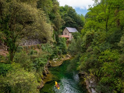 Kanovaarders op een groene rivierkloof in de Picos de Europa, met een huis tussen het bos.
