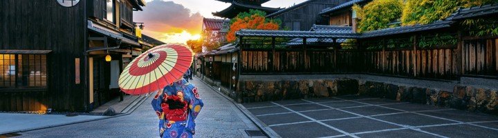 Vrouw in kimono met parasol in de straten van Gion, Kyoto, met pagode bij zonsondergang.