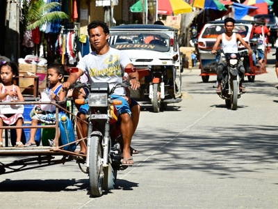 Motor met zijspan in een straat in de Filipijnen, met kinderen als passagiers en kleurrijke parasols op de achtergrond.