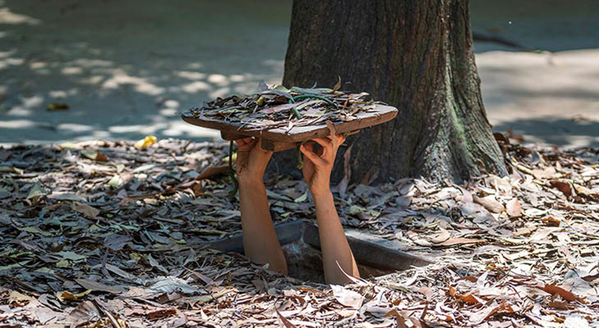 Handen steken uit een Vietnamees Cu Chi-tunnelgat en houden een camouflagedeksel vast.