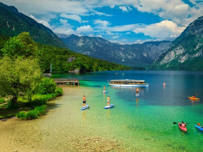 Suppen en kajakken op het heldere water van het Meer van Bohinj in Slovenië, met bergen op de achtergrond.