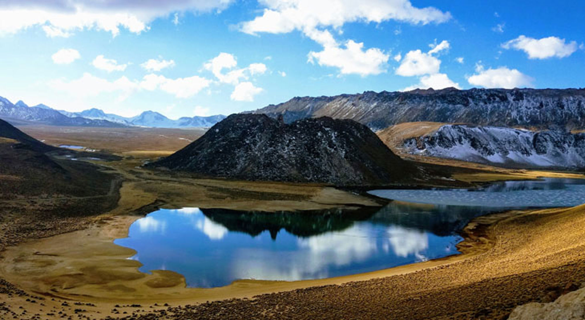 Huaraz Hooggelegen bergmeer in Peru met weerspiegeling van wolken, omringd door ruige bergen en een vulkanische heuvel.