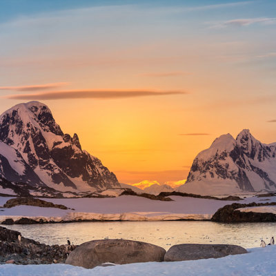 Zonsondergang boven besneeuwde bergen en zee-ijs in Antarctica tijdens een groepsrondreis per vliegtuig.
