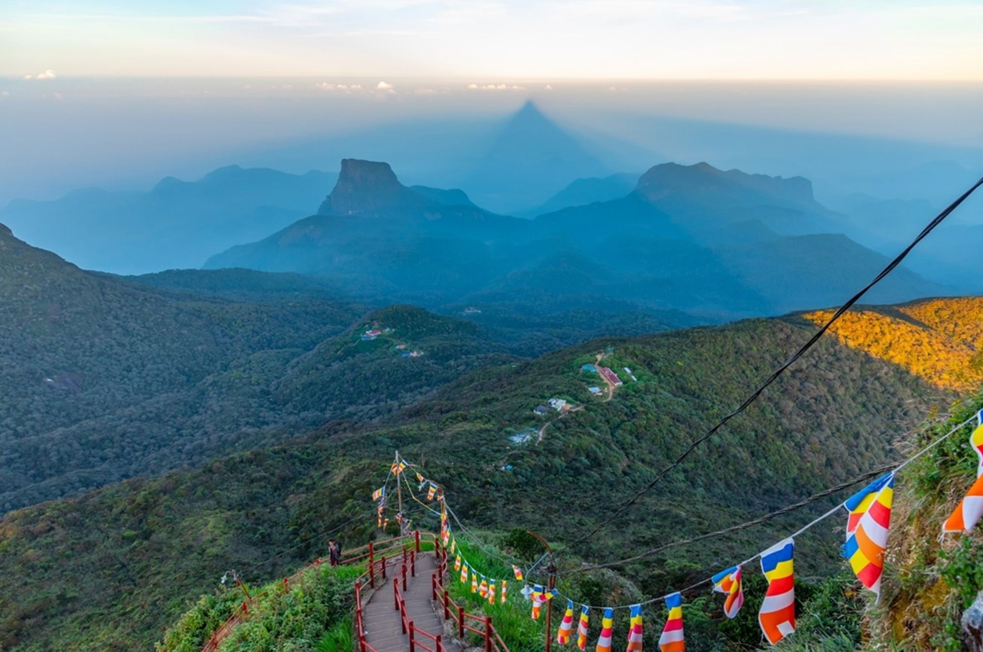 Uitzicht vanaf Adam’s Peak op de bergketens van Sri Lanka bij zonsopgang, met gebedsvlaggen langs het pad.