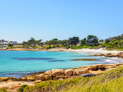 Kustlandschap in Australië met turquoise zee, rotsen en wit zandstrand onder een heldere blauwe lucht.