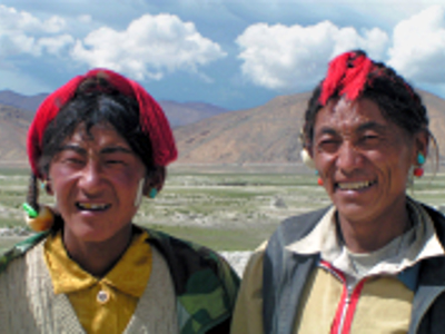 Twee lachende Tibetanen met traditionele rode hoofdbedekking in het berglandschap van Tibet en Nepal.