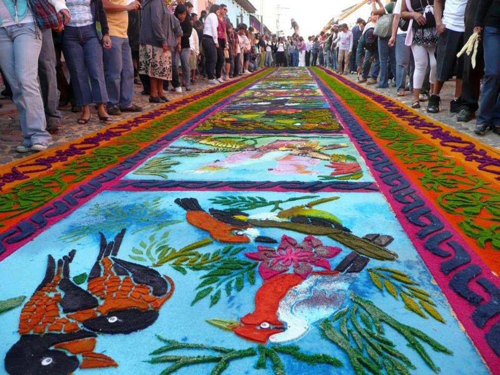Gekleurde zaagselstraatkunst tijdens een processie in Guatemala, met toekans en bloemenmotieven.