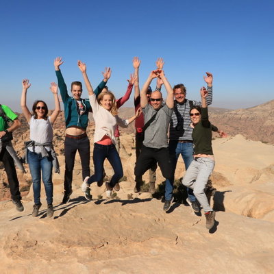 Groepsrondreis Jordanië: reizigers springen juichend op rotsen met uitzicht over het woestijnlandschap.