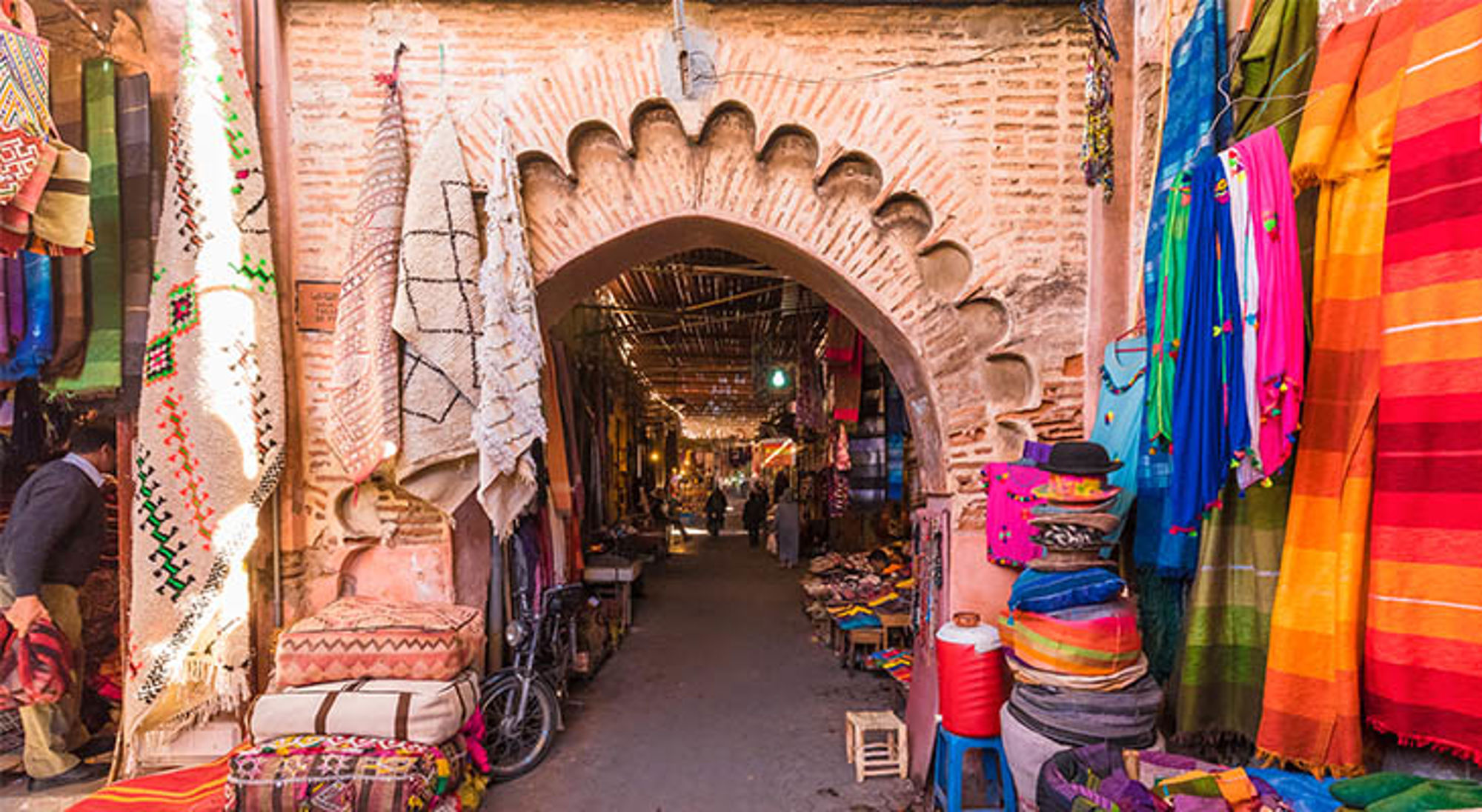 Toegangspoort tot een Marokkaanse souk met kleurrijke tapijten en textiel te koop.