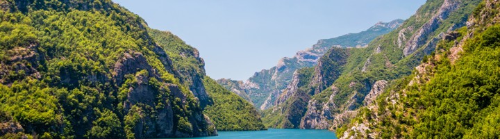 Uitzicht op Koman Lake in Albanië, met turquoise water tussen groene bergen en rotskliffen.