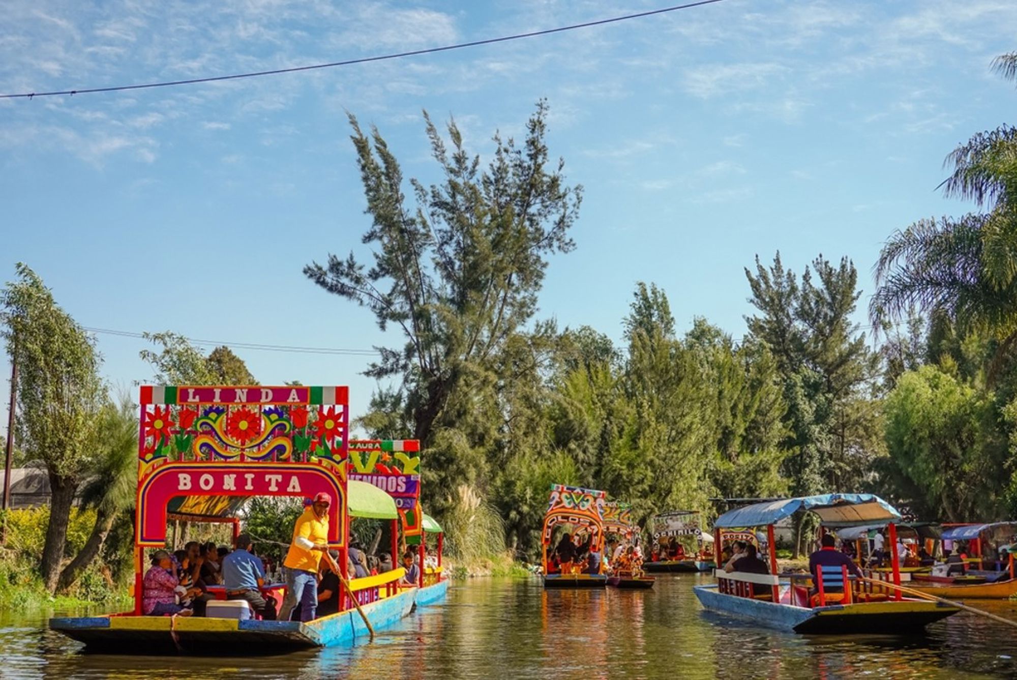 Kleurrijke trajineras op de kanalen van Xochimilco in Mexico-Stad, met passagiers tussen groene oevers.