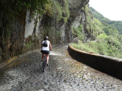 Fietser op de Ruta de las Cascadas bij Baños, Ecuador, langs een rotswand met waterval.