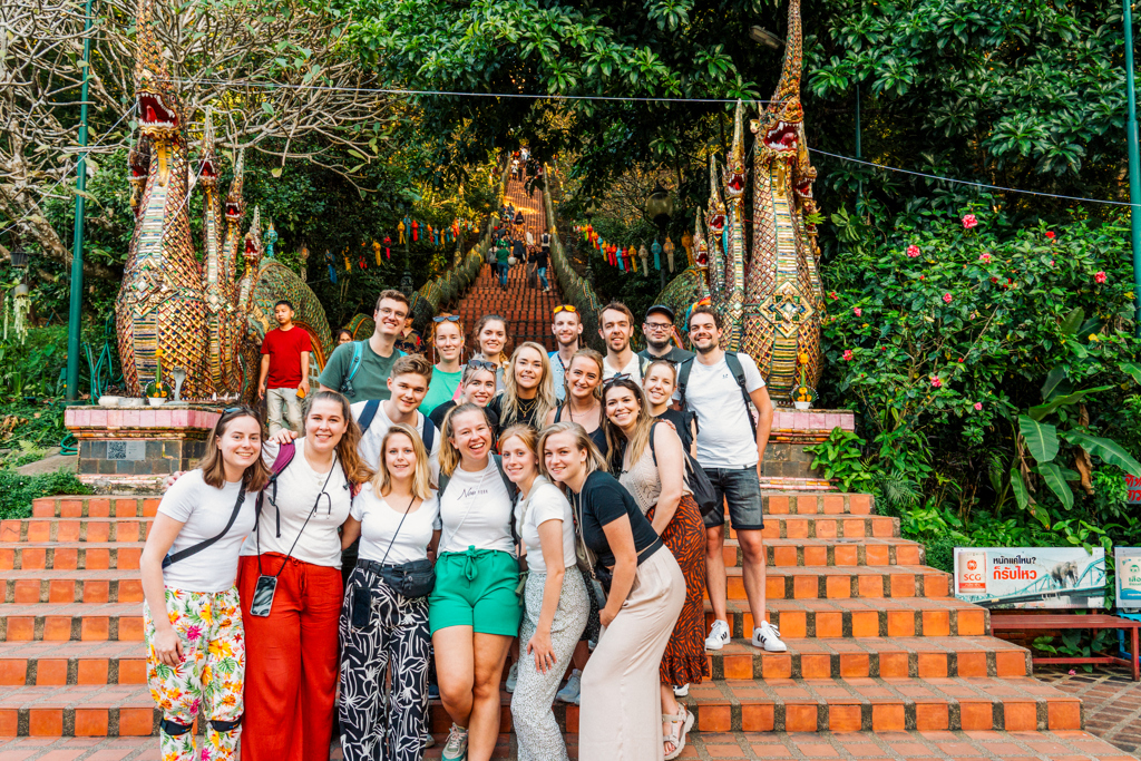 Groepsfoto van 22-35ers reis Thailand bij tempeltrap met naga-beelden in het groen.