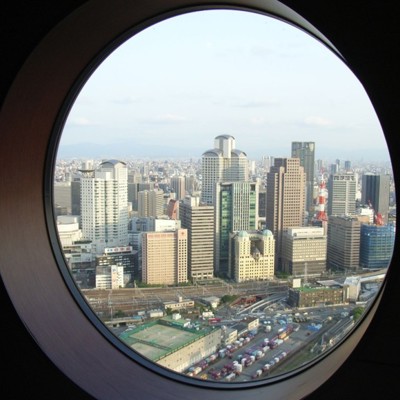 Uitzicht op de skyline van Osaka door een rond raam, tijdens een groepsrondreis Japan hoogtepunten.