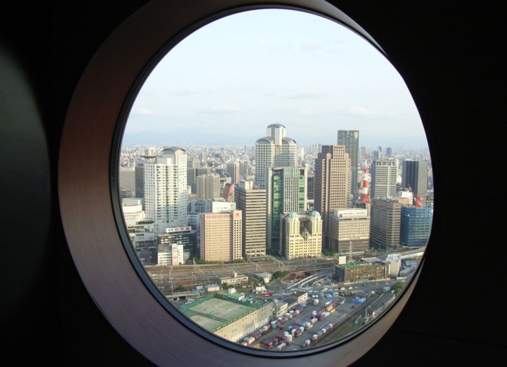 Uitzicht op de skyline van Osaka door een rond raam, tijdens een groepsrondreis Japan hoogtepunten.