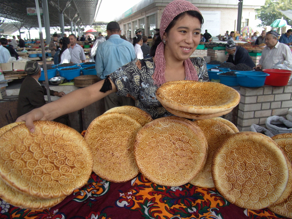 Marktvrouw met traditioneel rond brood op een markt langs de Zijderoute tijdens een groepsrondreis.