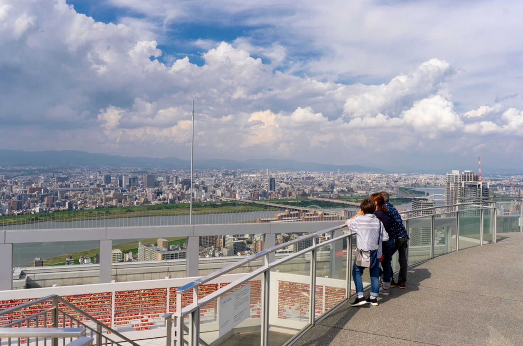 Uitzicht over Osaka vanaf een observatiedek, met bezoekers aan de reling en de rivier in de verte.