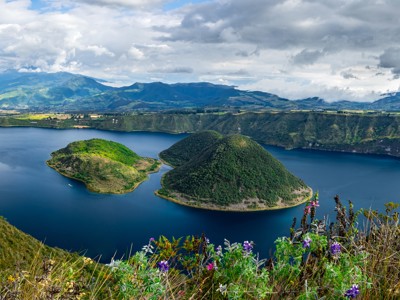 Uitzicht op het Cuicocha-kratermeer in Ecuador met groene eilandjes en bergen onder een bewolkte lucht.