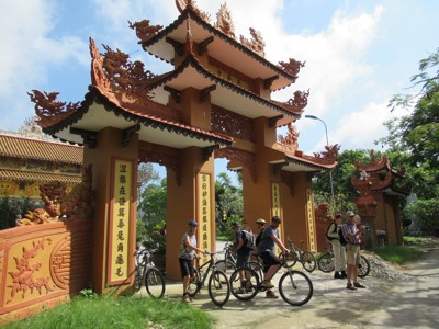 Fietsers bij een sierlijke tempelpoort met drakenornamenten tijdens de Route Vietnam.