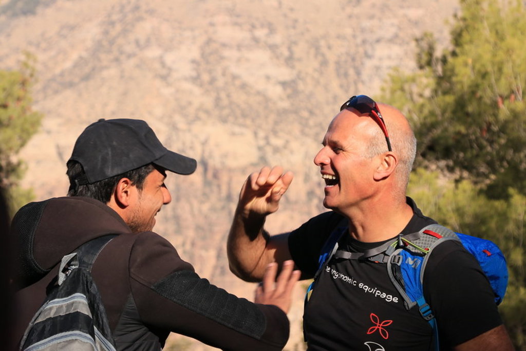 Twee wandelaars lachen samen tijdens een groepsrondreis in Jordanië, met rotsachtig berglandschap op de achtergrond.