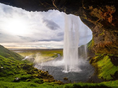 Waterval Seljalandsfoss in IJsland, gezien van achter de watergordijn met groen landschap en kustvlakte.