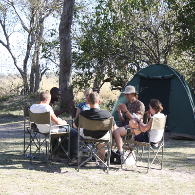 Reizigers spelen kaarten bij een kampeerplek met tenten in Zuidelijk Afrika tijdens familiereis Namibië, Botswana en Zimbabwe.