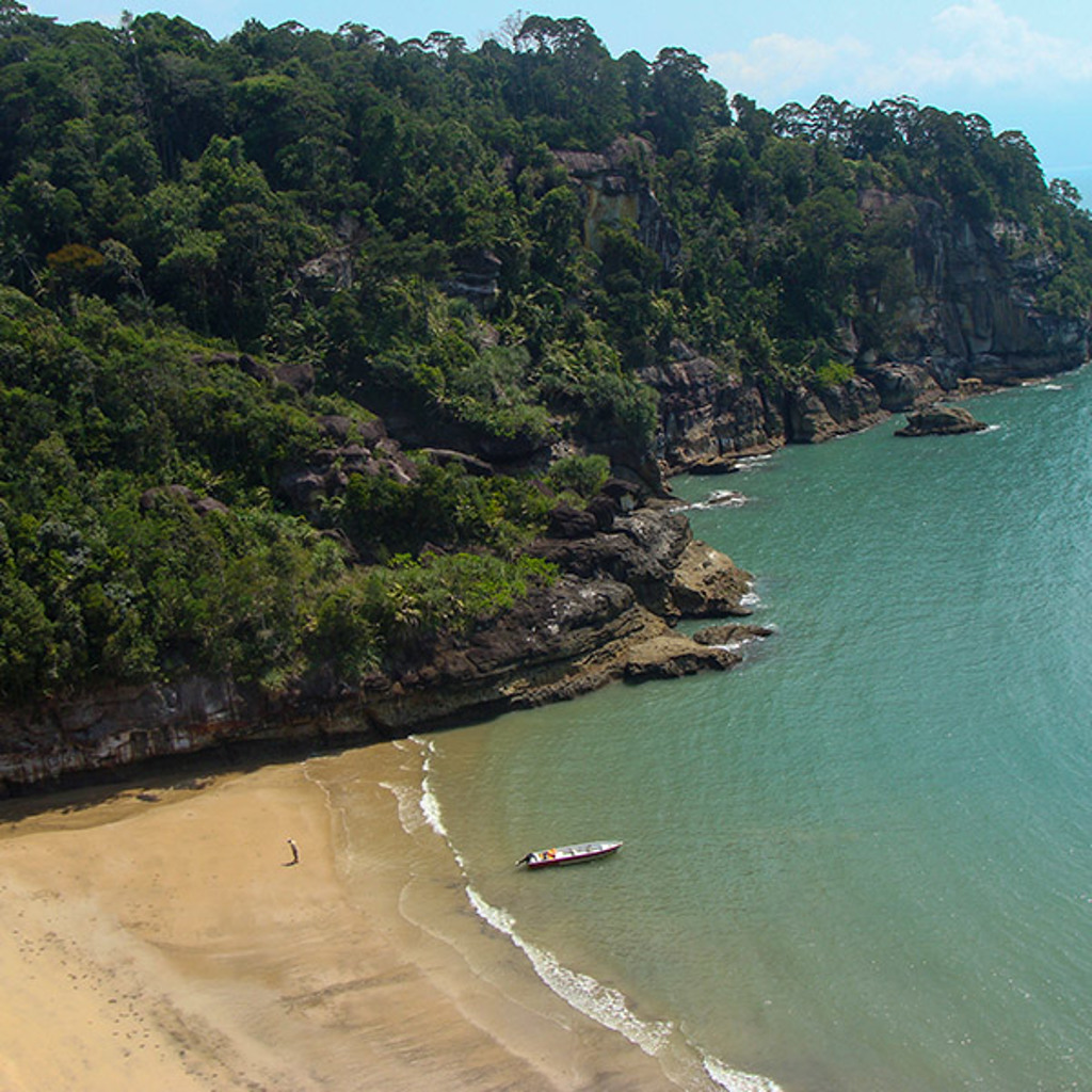 Groene kust met rotsen en strand in Maleisisch Borneo, met bootje op zee.