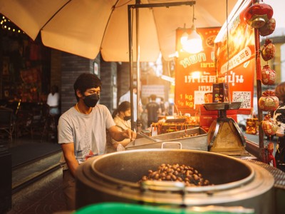 Straatverkoper op avondmarkt in Thailand roostert kastanjes bij een kraam met Thaise borden en lampen.