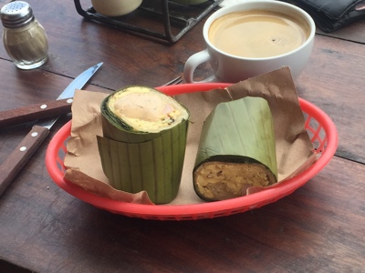 Mexicaans ontbijt met tamales in bananenblad en een kop koffie op een houten tafel.