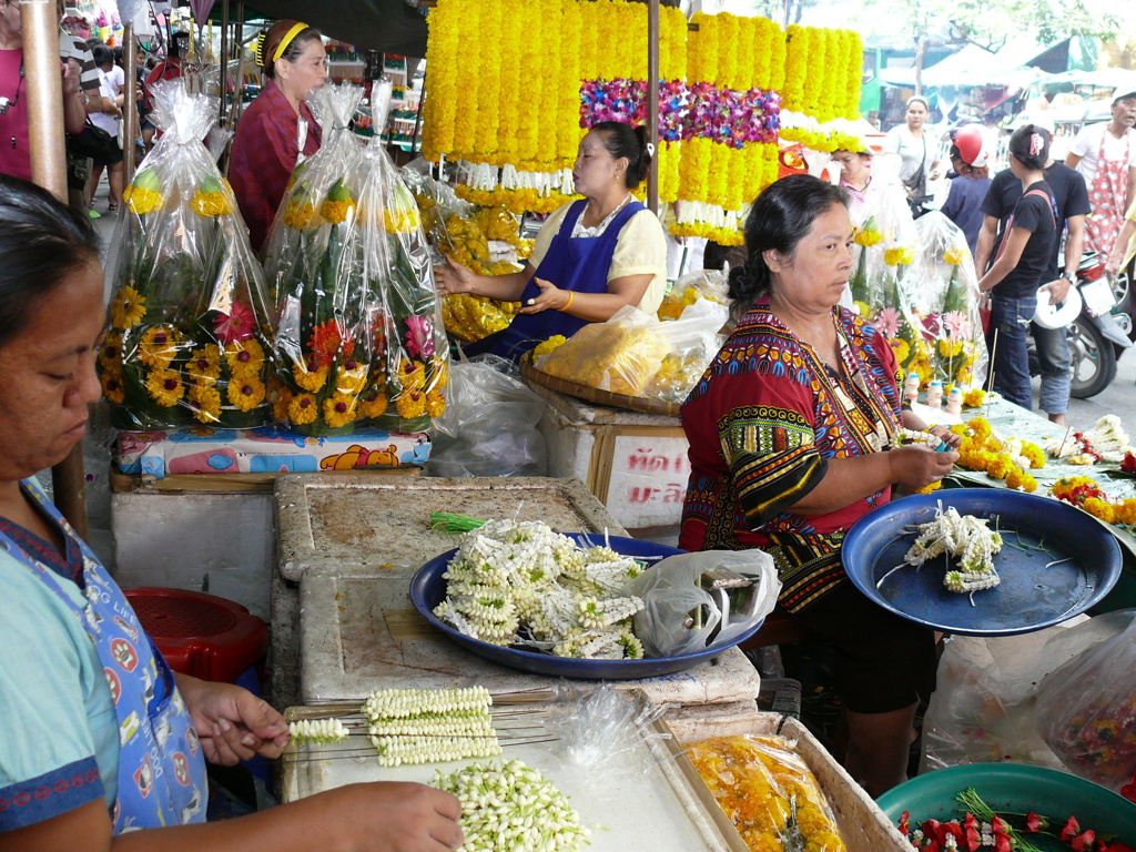 Bloemenmarkt in Thailand met verkopers die jasmijnkransen en gele bloemenkransen maken en verkopen.