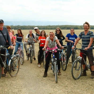 Groep fietsers tijdens familiereis in Tanzania, met savanne en bergen op de achtergrond.