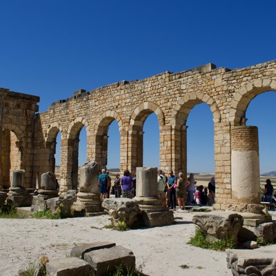 Groepsreis Marokko: bezoekers bij de Romeinse ruïnes van Volubilis met stenen bogen en zuilen.