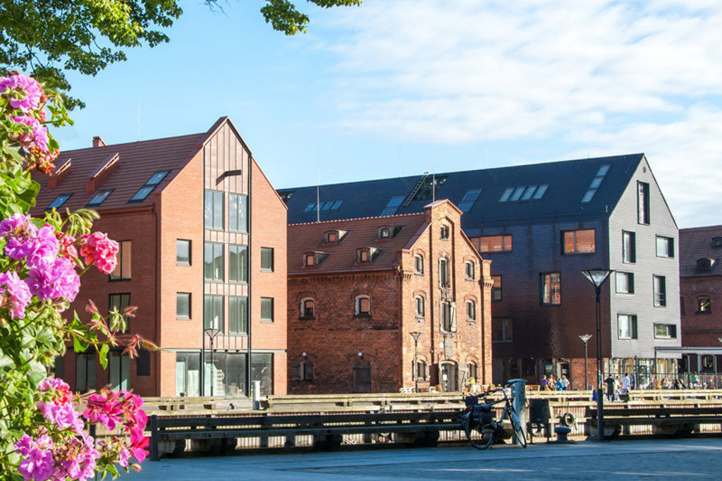 Gerestaureerde pakhuizen aan de rivier in Riga, Letland, met moderne gevels en terras aan de kade.