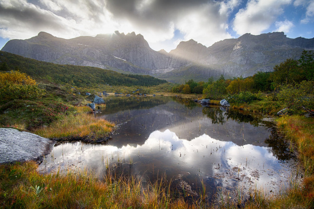 Berglandschap op de Lofoten met spiegelend meer en zonlicht door de wolken, Noorwegen.
